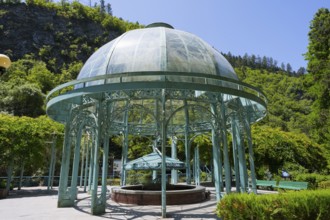 Metal glass pavilion surrounded by a green garden under clear summer sky, pavilion with mineral