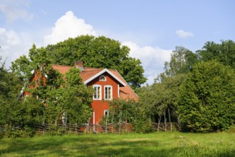 Charming red house with white windows, surrounded by trees and a wooden fence at the birthplace of
