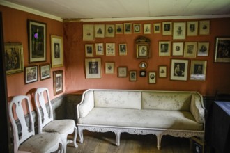 Historic living room with lots of framed pictures on the wall. An antique sofa and chairs stand on