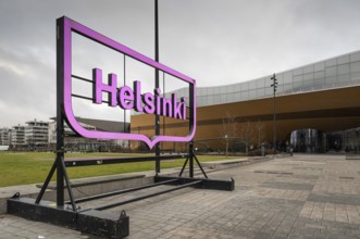 Large pink glowing Helsinki city logo, in front of Oodi Central Library and Cultural Center,