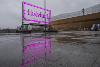 Large pink glowing city logo of Helsinki, in front of Oodi Central Library and Cultural Center,