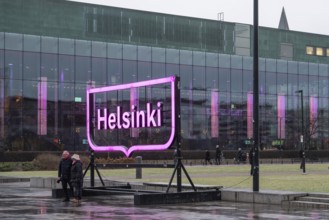 Tourists in front of Helsinki's big pink city logo, near Oodi Central Library and Cultural Center,