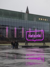 Tourists with selfie sticks take pictures of themselves in front of the glowing pink Helsinki city