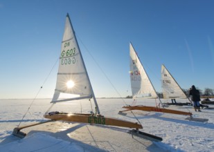 Three ice sailboats on frozen lake under clear blue sky and bright sunshine on frozen Dümmer,