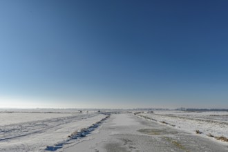 Snowy open landscape with wide sky and distant horizon under blue sky in the foreground the frozen