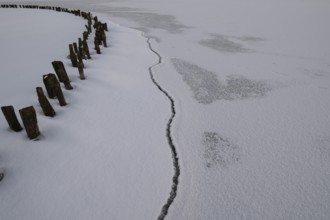 Frozen lake surface of Dümmer See with wooden posts and distinctive fault line in ice, frozen