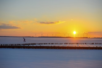 Ice skaters in front of sunset over icy landscape with wind turbines and intense colors on the