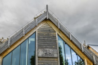 Modern building with wooden paneling and large glass windows under a cloudy sky, labelled as Café