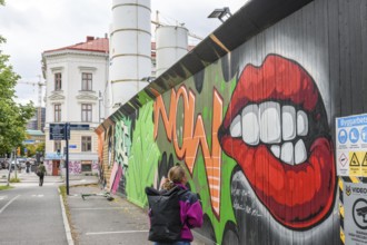 Colourful graffiti on an urban street scene with eye-catching lip motifs is viewed by a young