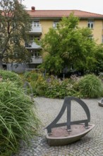 Green garden with art installations and lush plants in front of a residential building, Gothenburg,