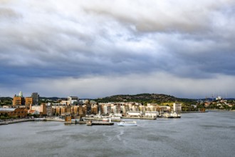 Urban landscape with waterside buildings and hills in the background under cloudy sky, Gothenburg