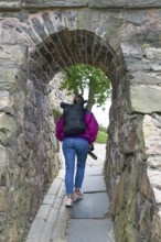 Person passes an old stone arch, a mix of history and nature in an exploration setting,