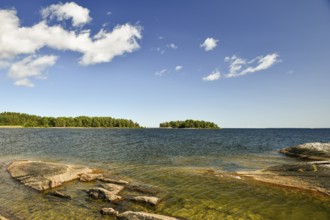 A lake with rocks in the foreground, islands on the horizon and a sky with few clouds at Lake