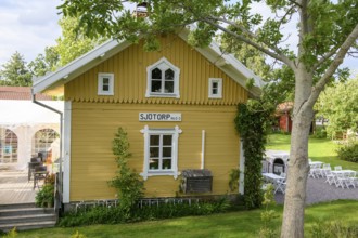 A yellow Scandinavian-style house with garden and benches on the Göta Canal, surrounded by trees on