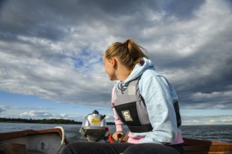 Young woman in a boat with outboard on the quiet lake Vänern, looking into the distance, the sky is