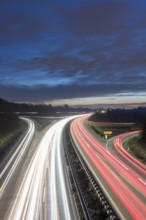 Long-exposure highway at night with light trails and cloudy sky over the countryside, near