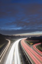 Night view of a motorway with red and white light trails against a cloudy sky, near Stuttgart,