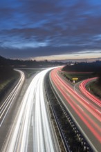Long-exposure view of a motorway at night with continuous light trails on a blue sky, near