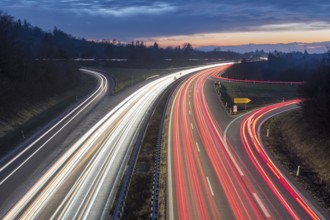 Highway view at dusk with red and white light trails, in front of an evening horizon, near