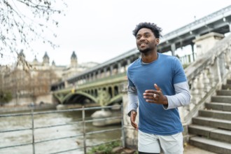 Young black man jogging along the seine in paris, training by the pont de bir hakeim with city