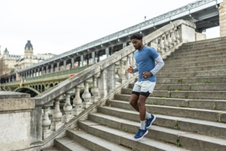 Young black man performing urban jogging and fitness training, actively descending large stone