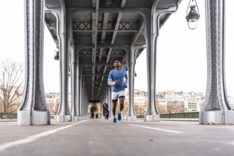 Young man jogging across bir hakeim bridge in paris, energetic urban workout against metal