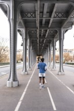 Person running along a dedicated path under the iconic metal structure of the bir hakeim bridge,