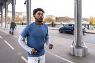 Young black man training on bir hakeim bridge in paris, jogging along the seine during a morning