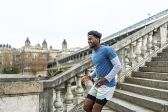Young black man in sportswear training, laughing, and running up concrete stairs on the bir hakeim