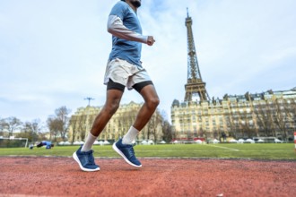 African american man sprinting on a red outdoor track in paris with the eiffel tower in the