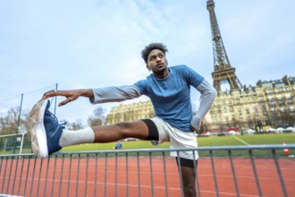 Young black man stretching legs on a paris running track before a workout, eiffel tower and