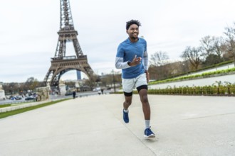 Athletic man jogging past the eiffel tower in paris, smiling and staying fit outdoors on a cloudy