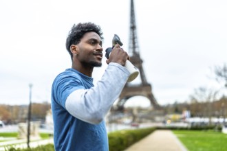 Young athletic man hydrating after a workout, holding a water bottle with the eiffel tower in the