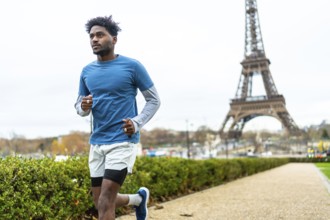 Young black man jogging along a path in a park with the eiffel tower in the background, focusing on