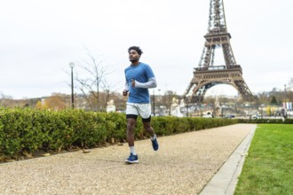 Young man actively jogging along a pathway in a parisian park, focusing on health and fitness with