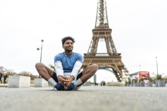 Young black man doing a butterfly stretch on paris pavement, warming up for urban run with the