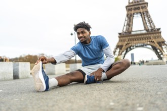 Young black man stretching on the ground, preparing for exercise with the iconic eiffel tower in