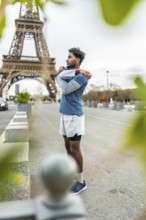 Young athletic man stretching his arms and shoulders on a city street in paris, preparing for an
