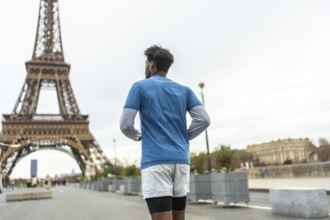Adult man with dark skin running and training in the city of paris with the famous eiffel tower in