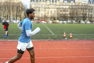 Sporty young black man running on an outdoor track in a stadium, focusing on fitness and urban