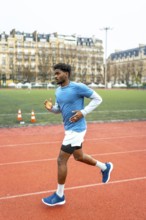 Young dark skinned athlete sprinting on a red urban track in paris, full body side view capturing