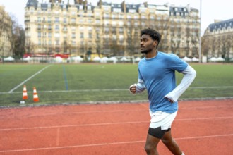 Young black man training on a running track with historic parisian buildings in the background,