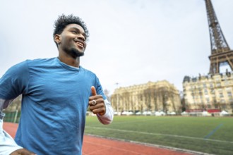 Young black man smiling and jogging outdoors on a running track with the iconic eiffel tower and