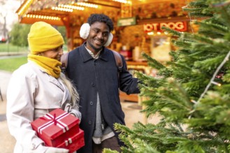 Joyful multiethnic couple holding red gifts, smiling as they stroll a festive paris christmas