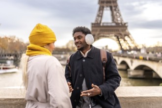 Diverse couple enjoying a romantic winter getaway in paris on a bridge by the eiffel tower,