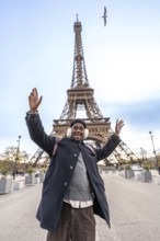 Young man with winter earmuffs raising arms in excitement and smiling widely while visiting the