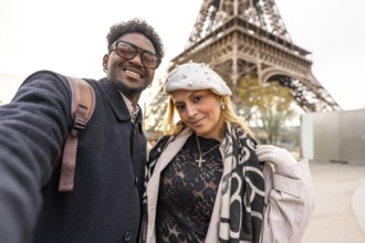 Diverse couple smiling for a close up selfie in front of the eiffel tower, embracing travel and
