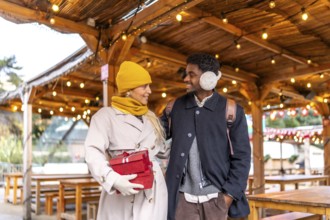 Diverse couple walking together and exchanging smiles in a festive outdoor christmas market in