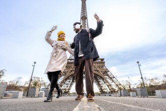 Happy young couple dancing with raised hands on a paris street by the eiffel tower, enjoying a