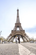 Couple holding hands walking down a street with a white line towards the eiffel tower on a bright
